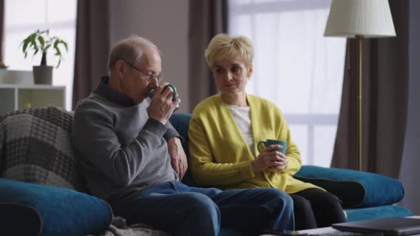 stařec a žena odpočívají o víkendu doma, důchodci popíjejí čaj na gauči v obývacím pokoji - Záběry, video