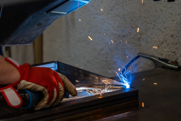 Mann schweißt Stahlrahmen in Werkstatt für Fälschung und Metallverarbeitung - Foto, Bild