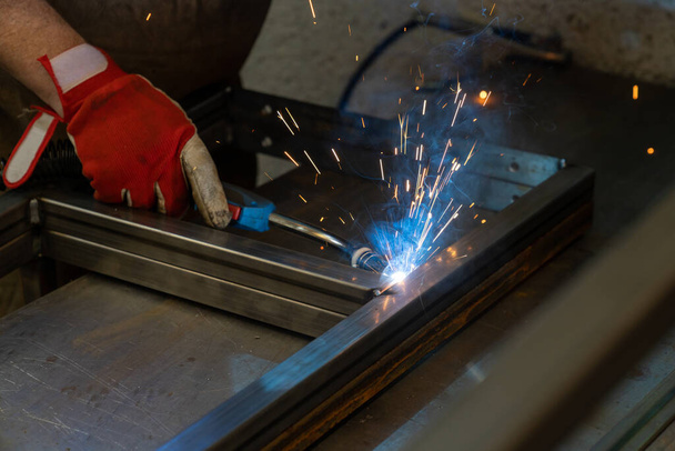 Hombre soldadura de marcos de acero en un taller de falsificación y trabajos de metal - Foto, Imagen