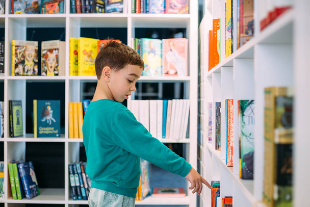 Malý chlapec sáhne po poličce s dětskými knihami v knihkupectví. - Fotografie, Obrázek
