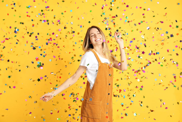 Happy woman and falling confetti on yellow background - Foto, Bild