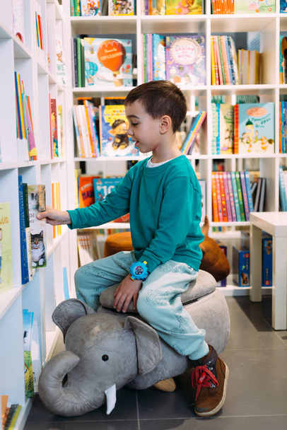 Ein kleiner Junge greift nach einem Regal mit Kinderbüchern in der Buchhandlung. - Foto, Bild