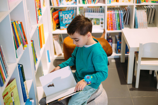 Pieni poika kurkottaa hyllylle lastenkirjoja kirjakaupassa.. - Valokuva, kuva