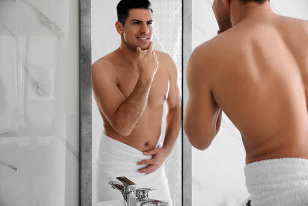 Hezký muž dotýká jeho hladký obličej po holení v blízkosti zrcadla v koupelně - Fotografie, Obrázek