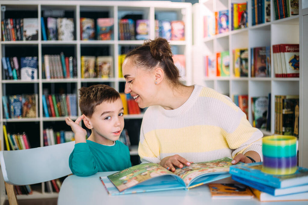 Η μαμά και το μικρό της παιδί, ο γιος του νηπιαγωγείου, διαβάζουν μαζί παιδικά βιβλία. - Φωτογραφία, εικόνα