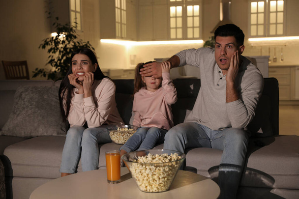 Family watching movie with popcorn on sofa at night - Photo, image