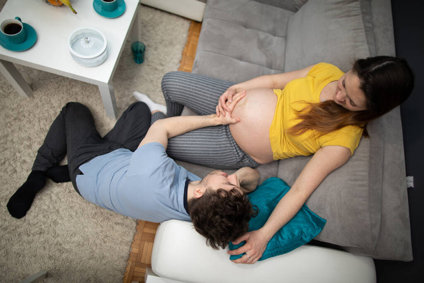 Echtgenoot omarmt zwangere vrouwen buik en ze glimlachen naar elkaar. Vrouw in een gevorderde zwangerschap. Uitzicht van bovenaf. - Foto, afbeelding