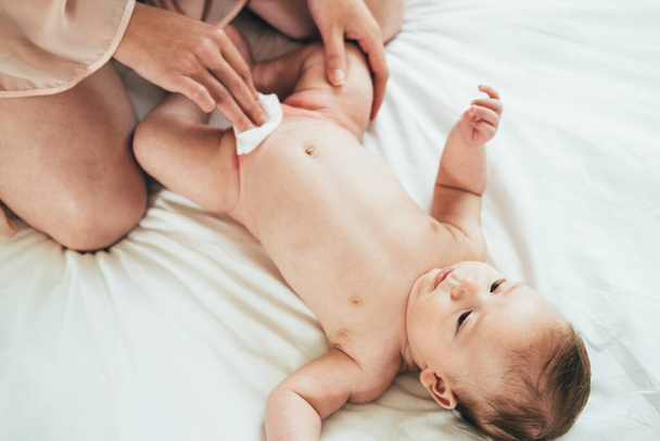 Anya törlése Kicsi baba Baby Wipeand pelenka cseréje HomeHigh Ange kilátás aranyos újszülött baba kapok egy pelenka csere az ágyban. - Fotó, kép