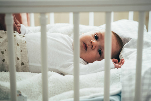 Cute Baby Lying in the Crib and Looking at CameraBeautiful little baby boy relaxing in his crib at home. - Фото, изображение