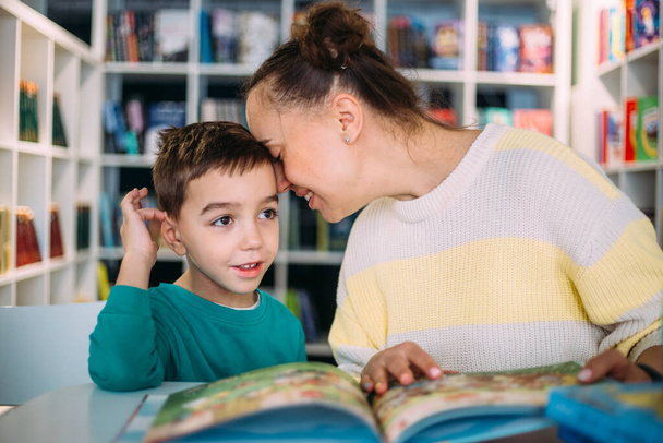 Η μαμά και το μικρό της παιδί, ο γιος του νηπιαγωγείου, διαβάζουν μαζί παιδικά βιβλία. - Φωτογραφία, εικόνα