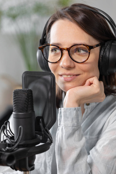 A fashionable European woman wearing headphones and a microphone records a podcast or radio show, a Caucasian woman creates audio content for her blog or podcast or records her voice for an audiobook - Photo, Image