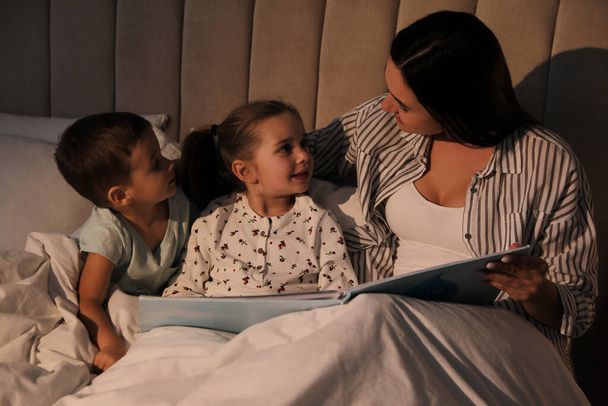Mother reading bedtime story to her children at home - Фото, изображение
