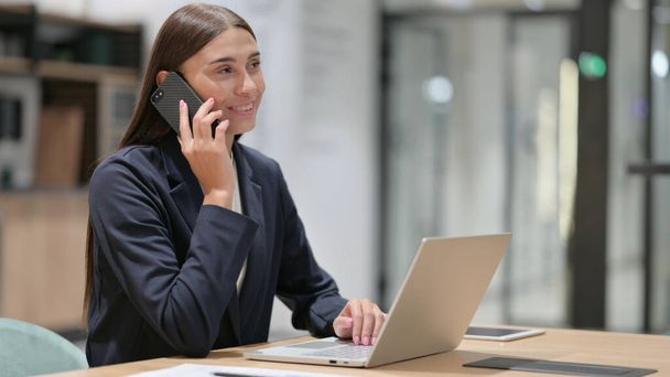 Businesswoman with Laptop Talking on Phone in Office  - Foto, afbeelding