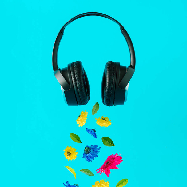 Advertisement idea with black music headphones, colorful summer flowers and green leaves against pastel blue background. Minimal nature concept. - Photo, image