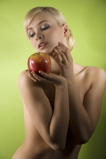 fashion and glamour shot of a dreaming nude young woman with red apple on green background - Fotografie, Obrázek
