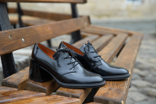 レディースレザーブーツクローズアップ。木製のベンチに黒い光沢のあるオックスフォードスタイルの靴 - 写真・画像