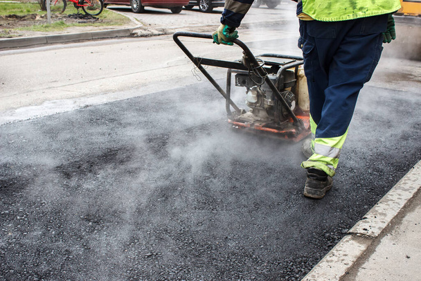 lavoratore rampe l'asfalto sulla strada con un costipatore meccanico. posa del manto stradale. asfalto caldo sotto la pressione del costipatore - Foto, immagini