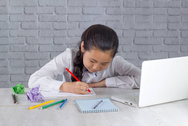Little Asian girl studying from home in an online classroom learning online video call. She attends online school lessons with a laptop and takes notes at home. New normal. Staying at home. - 写真・画像