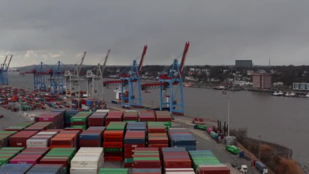 Niedrige Luftaufnahme von Frachtkranen und bunten Containern am Fluss im Hamburger Hafen - Filmmaterial, Video