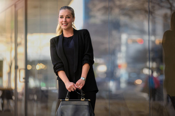 Retrato franco de una joven mujer de negocios bonita y hermosa en un traje elegante y de moda, sosteniendo un costoso bolso de diseñador  - Foto, imagen