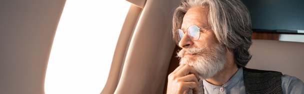 Uomo maturo con gli occhiali che guarda il finestrino dell'aereo, striscione  - Foto, immagini