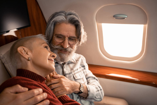 maduro hombre abrazando sonriente esposa en privado jet  - Foto, Imagen