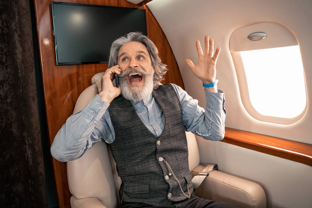 Excited businessman talking on cellphone in private airplane  - Foto, afbeelding