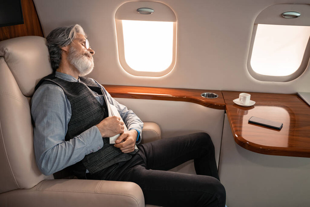 Homme d'affaires mature avec magazine dormant près de tasse et smartphone en jet  - Photo, image