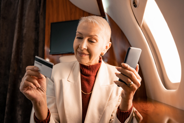 Mosolygó üzletasszony kezében hitelkártya és okostelefon kabin magánrepülőgép  - Fotó, kép