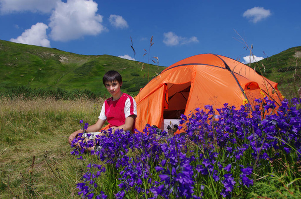 Tinédzser fiú lazít a narancssárga sátor mellett a táborban. Turisztikai tevékenység a szabadban. Nemzeti Vegyünk egy túra nap november 17-én - Fotó, kép