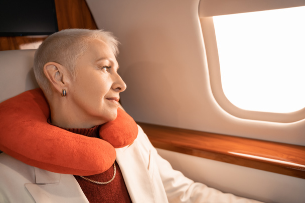 Femme d'affaires mature dans l'oreiller du cou regardant la fenêtre de l'avion  - Photo, image