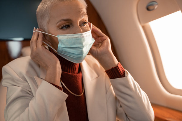 Mature businesswoman wearing medical mask in plane  - Фото, изображение