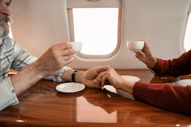 Érett pár csészék fogják egymás kezét a magánrepülőn  - Fotó, kép