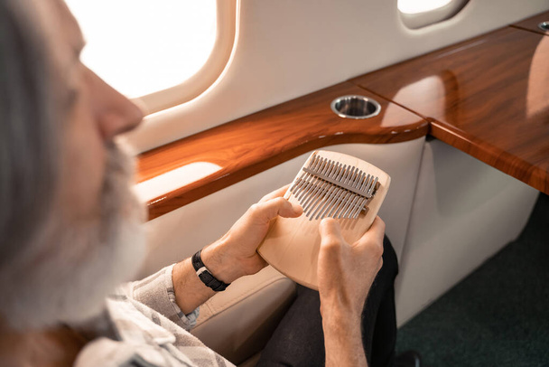 Mbira em mãos de homem maduro em primeiro plano desfocado em avião privado  - Foto, Imagem