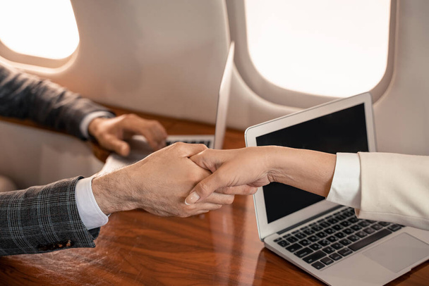 Vágott kilátás üzletemberek kezet rázás közelében laptopok a repülőn  - Fotó, kép