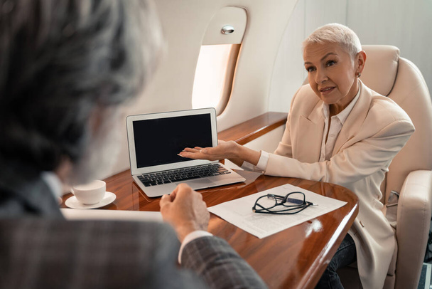 Femme d'affaires pointant avec la main à l'ordinateur portable près du document et homme d'affaires dans l'avion  - Photo, image