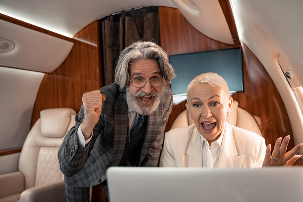 Gente de negocios emocionados mirando borrosa portátil en avión privado  - Foto, Imagen