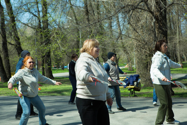 Dnepropetrovsk,ウクライナ- 04.22.2021:公園で健康とフィットネス体操を行う高齢者のグループ.老人はテニスボールとラケットの練習を行う. - 写真・画像