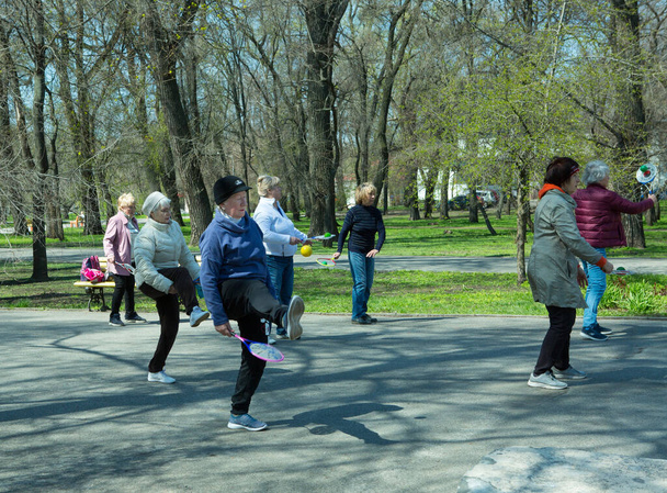 Dnepropetrovsk, Ukraina - 04.22.2021: Ryhmä eläkeläisiä tekemässä kuntovoimistelua puistossa. Vanhat miehet tekevät tennispallo- ja mailaharjoituksia. - Valokuva, kuva