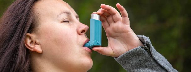 Mooie jonge brunette vrouw die astma inhalator gebruikt tijdens een sterke astma aanval, farmaceutisch product wordt gebruikt om piepende ademhaling en kortademigheid te voorkomen en te behandelen, gezondheidszorg concept - Foto, afbeelding