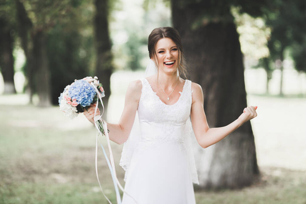 Beautiful bride in elegant white dress holding bouquet posing in park - Fotoğraf, Görsel
