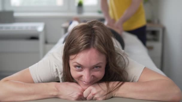 Une femme heureuse montre un signe cool tout en massant ses jambes sur une table de massage - Séquence, vidéo