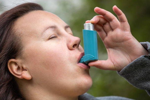 Jolie jeune femme brune utilisant un inhalateur d'asthme lors d'une forte crise d'asthme, le produit pharmaceutique est utilisé pour prévenir et traiter la respiration sifflante et l'essoufflement, concept de soins de santé - Photo, image