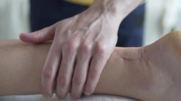 Le masseur frotte l'huile sur la jambe du patient avec une blessure à l'achille et commence le massage - Séquence, vidéo