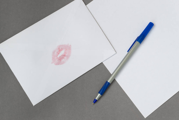 Vaaleanpunainen huulipuna suudella valkoinen kirjekuori, paperiarkki kynä harmaalla pohjalla. Rakkauskirje - Valokuva, kuva