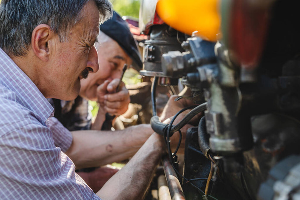 Dva kavkazský senior muži otec a syn důchodce na farmě opravy traktor stroj v slunečný den rodina lepení generace spolupráce a koncepce sounáležitosti skuteční lidé - Fotografie, Obrázek