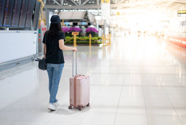 アジアの女性が荷物スーツケースを持ち、手術用マスクを着用して空港でチケット搭乗券を取得するためのチェックインの準備をします。コビト19の流行の間に.  - 写真・画像