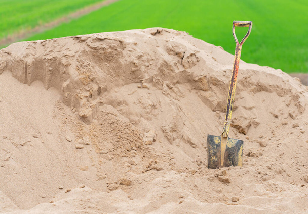 Egy ásó beragadt egy halom homokba, amit építkezésre használtak a mezőn.. - Fotó, kép