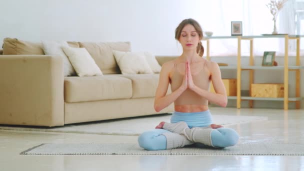 Menina esportiva atraente sentado em posição de lótus com as mãos em namaste. Menina fazendo ioga com os olhos fechados - Filmagem, Vídeo