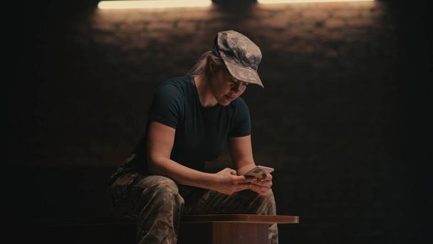 Sotilaallinen nainen käyttää älypuhelinta pimeässä huoneessa - Valokuva, kuva